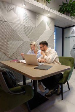 İki birey modern bir ofiste dizüstü bilgisayarla birlikte çalışıyor.