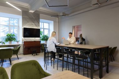 İki iş arkadaşı modern mobilyalarla bir ofis ortamında tartışıyorlar..