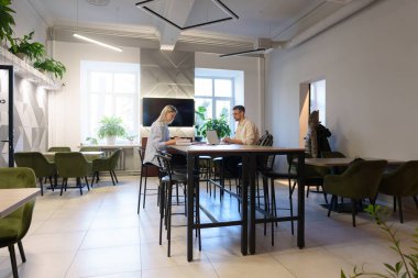 Yeşil sandalyeler, bitkiler ve iş projeleriyle uğraşan bireylerin yer aldığı çağdaş ofis alanı