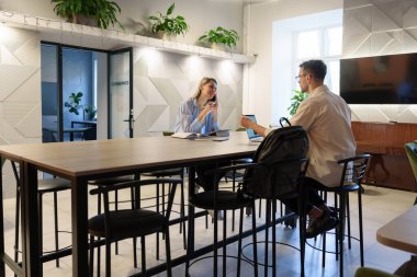 İki profesyonel, iyi ışıklandırılmış, çağdaş bir ofis alanında bir masada iş birliği yapıyor..