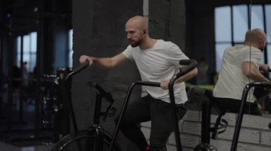 Spor salonunda bisiklete binen, sıkı çalışan ve müzik dinleyen bir adam..