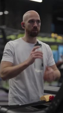 Spor salonunda koşu bandında su içen bir adam. Fitness, sağlık ve hidrasyon.
