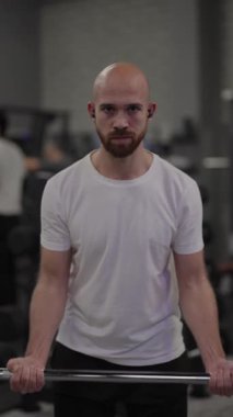 Sakallı kel adam spor salonunda ağırlık kaldırıyor..