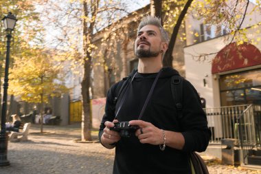 Sonbahar manzarasıyla çevrili şehir merkezinde kameralı bir adam.