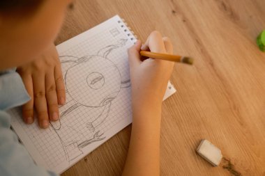 Bir çocuk çizim kağıdına bir karakter çizmek için kalem kullanır, yaratıcılık ve odaklanmayı gösterir. Yakın çekim görüntüsü onların sanat eserlerinin detaylarını ve kullanılan araçları yakalar.