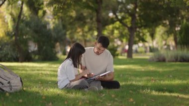 Bir liseli kız ve babası bir parkta çimlerin üzerinde oturuyorlar, okuldan sonra birlikte ödevlerini yapıyorlar..