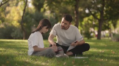 Şefkatli bir baba, kızına parkta ev ödevlerinde yardım eder. Ailesinin desteğini ve eğitimini gösterir..