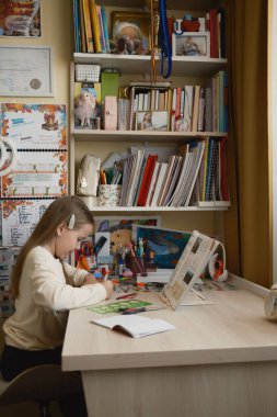 Genç bir kız, çeşitli sanat malzemeleri, kitaplar ve dekorasyonlarla organize bir masada yaratıcı faaliyetlerine yoğunlaşarak öğrenme, yaratıcılık ve çocukluk merakını aktarıyor..