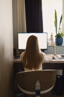 Uzun saçlı genç bir kız bilgisayar ekranına odaklanmış bir masada oturuyor..