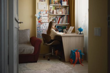 Bir çocuk rahat bir odada bir masada oturuyor, kitaplar, çizelgeler ve bir dünya arasında okuyor, öğrenme ve eğitim ortamı sergiliyor..