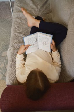 Kanepede uzanmış, sakin bir ortamda kitap okuyan bir insan. Sahnede rahatlık ve rahatlık vurgulanıyor, rahatlama ve ev aktiviteleriyle ilgili konular için mükemmel.