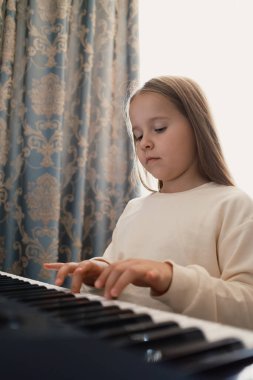 Genç bir kız perdeleri olan iyi ışıklandırılmış bir odada piyano çalma pratiği yapıyor. Sahne, o müzik becerilerini geliştirirken odak ve kararlılığını gösteriyor. Sıcak ve ilham verici bir ev ortamı..