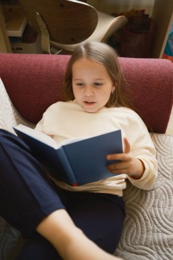 Genç bir kız kitap okurken rahatça evde oturur ve anın tadını çıkarır..