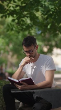 Genç bir adam parkta bir bankta oturuyor, kendini kitabına kaptırmış, okurken notlar alıyor..