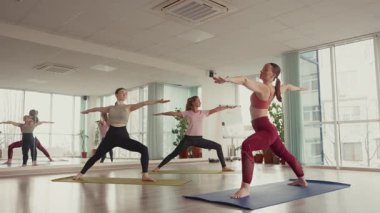 Stüdyoda yoga yapan üç kadın doğal ışıkla poz veriyor, sağlıklı yaşam için teşvik ediyorlar..