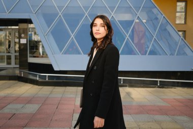 Şehir ortamında modern bir binanın arka planına güvenle karşı duran genç kadın