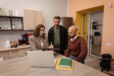 Gündelik ofis ortamında dizüstü bilgisayar kullanan üç kişi bir projede işbirliği yapıyor.