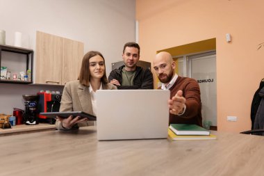 Şık bir ofiste dizüstü bilgisayarda birlikte çalışan üç profesyonel.