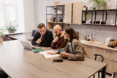Ofis mutfağındaki bir masada belgeleri analiz eden profesyonellerle ortak bir toplantı.