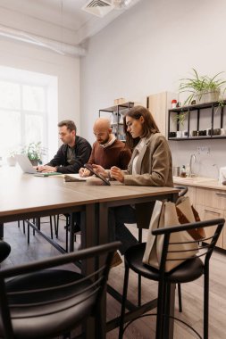 İş arkadaşları, iyi aydınlatılmış bir ofiste ortak çalışma oturumunda dizüstü bilgisayar ve tablet kullanıyorlar..