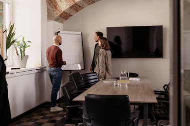 Meslektaşlar, şık bir iş yerinde, bir çizelgeyle fikir alışverişinde bulunuyorlar.