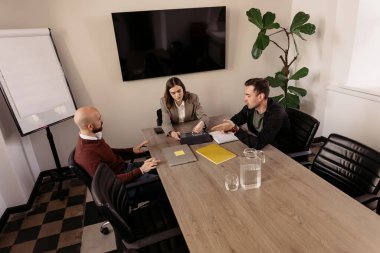 Ofis masasında evrak ve cihazlarla işbirliği yapan üç meslektaşım.