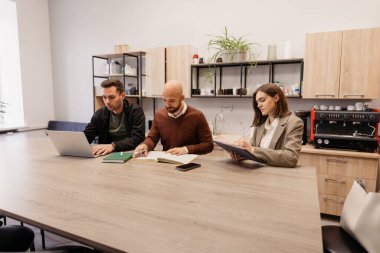 Çağdaş mobilyaları ve dekorasyonu olan bir ofiste üç kişi birlikte çalışıyor.