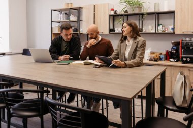 Modern bir işyeri mutfağındaki belgeleri incelerken iş arkadaşları birlikte iş birliği yapıyorlar..