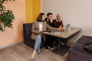 Modern bir ofis ortamında çalışırken üç iş arkadaşı bir projeyi tartışıyor.