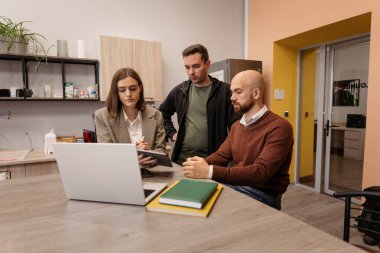 Ofiste dizüstü bilgisayarla bir projeyi tartışan üç meslektaşım var.