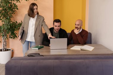 Üç profesyonel bir ofiste dizüstü bilgisayarla bir projeyi tartışıp planlıyorlar..