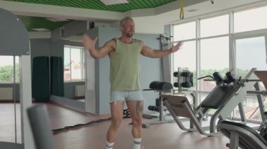 Yeşil kolsuz tişörtlü ve şortlu bir adam modern bir spor salonunda ısınma egzersizi yapıyor. Eğitim oturumuna hazırlanıyorum. Fitness ve sağlıklı yaşam tarzı konsepti.