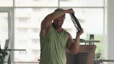 Modern bir spor salonunda ağırlık kaldırmaya odaklanmış bir adam. Ağırlık antrenmanı sırasında güç ve uygunluk göstergesi.