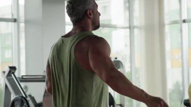Fitness için ip atlayan kaslı bir adamın dikiz görüntüsü. Adam iyi donanımlı, modern bir spor salonunda eğitim görüyor..