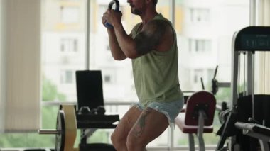Spor salonunda kettlebell çömelmesi yapan sıradan giyinmiş bir adam. Dayanıklılık eğitimi ve zindelik kavramı.