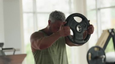 Parlak ışıklı bir spor salonunda ağırlık kaldıran kaslı bir adam güç, odaklanma ve zindelik gösteriyor. Sağlık ve refahı desteklemek için ideal imaj.