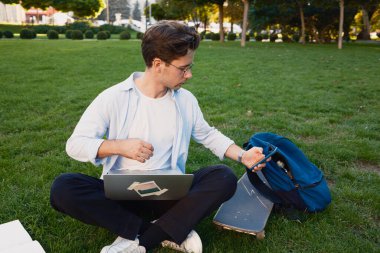 Parkta çimlerde dizüstü bilgisayarı ve kaykayıyla oturan bir adam sıradan ve üretken bir ana hitap ediyor..