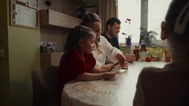 Aile evde iskambil oynuyor. Ebeveynler kızına öğretiyor.