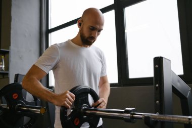 Spor salonunda halter hazırlayan bir adam camdan güneş ışığı alıyor.