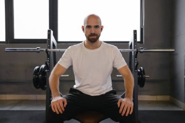 Adam ağırlık kaldırma ekipmanı ve kararlı bir ifadeyle spor salonunda oturuyor..