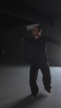 Genç bir kadın dans hareketlerini karanlık bir stüdyoda yapıyor..