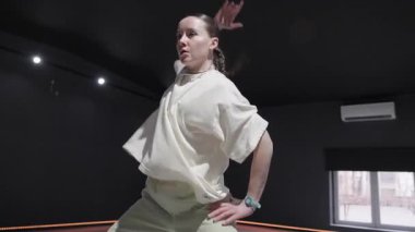 Siyah duvarlı bir stüdyoda tek başına dans eden genç bir kadın. Parlak ışıklarla aydınlatılır..