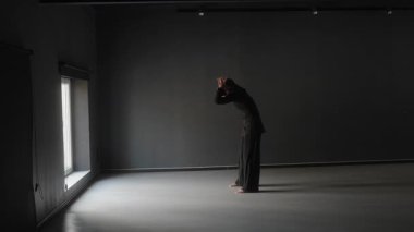 Pencerenin yanındaki karanlık odada tek başına dans eden genç bir kadın..