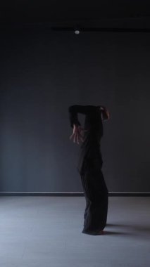 Siyah elbiseli zarif bir kadın karanlık bir stüdyoda dans ediyor..