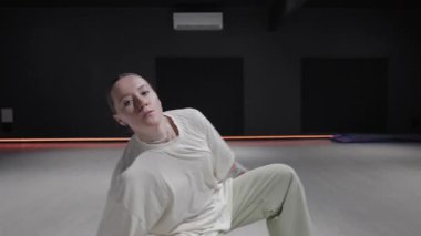 Karanlık bir stüdyoda turuncu aksanlı ışıklandırmayla dans eden genç bir kadın..