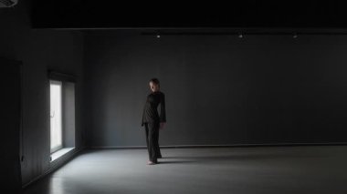 Karanlık bir stüdyoda tek pencereli genç bir kadın dans ediyor..