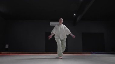 Karanlık duvarları ve turuncu ışıkları olan bir stüdyoda dans eden genç bir kadın..