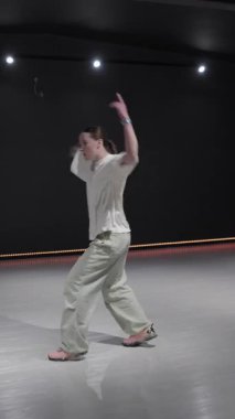 Stüdyoda dans eden genç bir kadın koyu arkaplan ve turuncu ışıklarla.