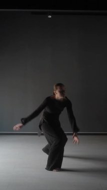 Genç bir kadın minimalist bir stüdyoda çağdaş bir dans sergiliyor..