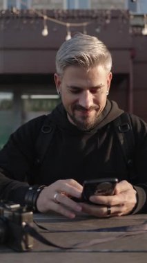 Neşeli adam dışarıda akıllı telefonunu kullanıyor, teknolojiyle bağlantı kuruyor ve keyfine bakıyor..